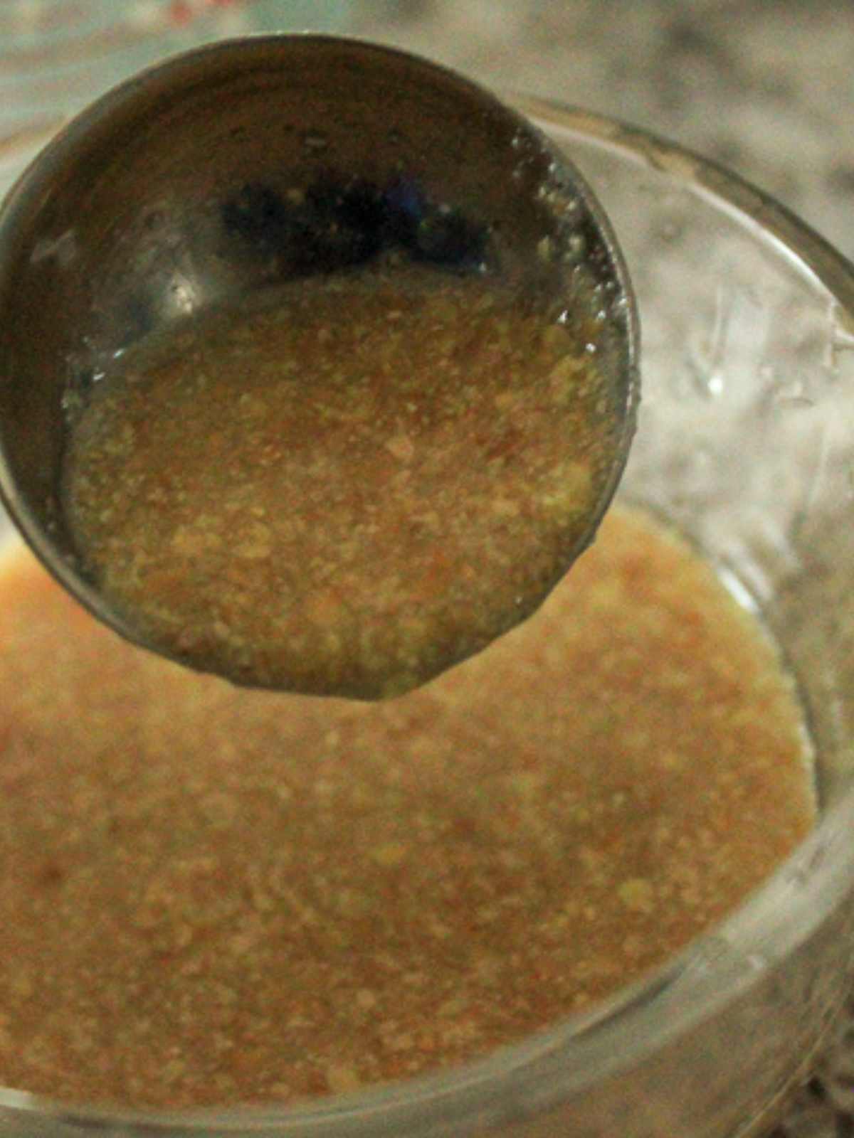Close up shot of a flax seed egg in a 1 tablespoon measuring spoon pouring into a small glass bowl of flax egg. 
