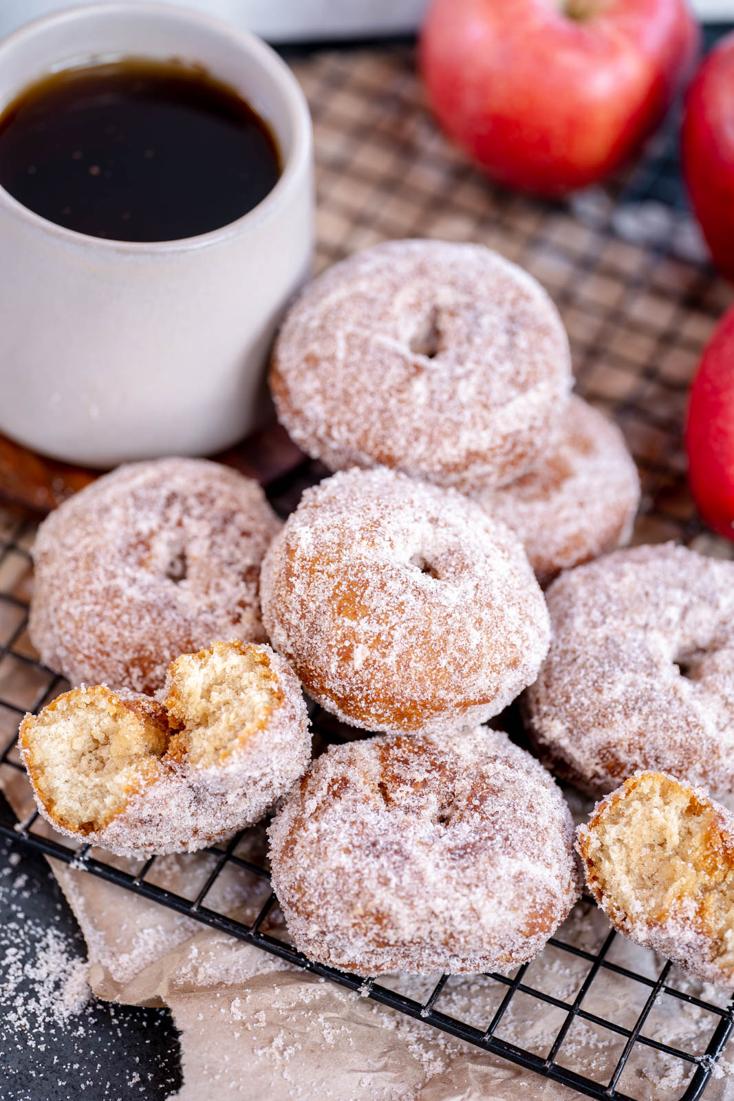 Vegan Apple cider donuts stacked in a pile with one donut cut in half on a black cooling rack. 