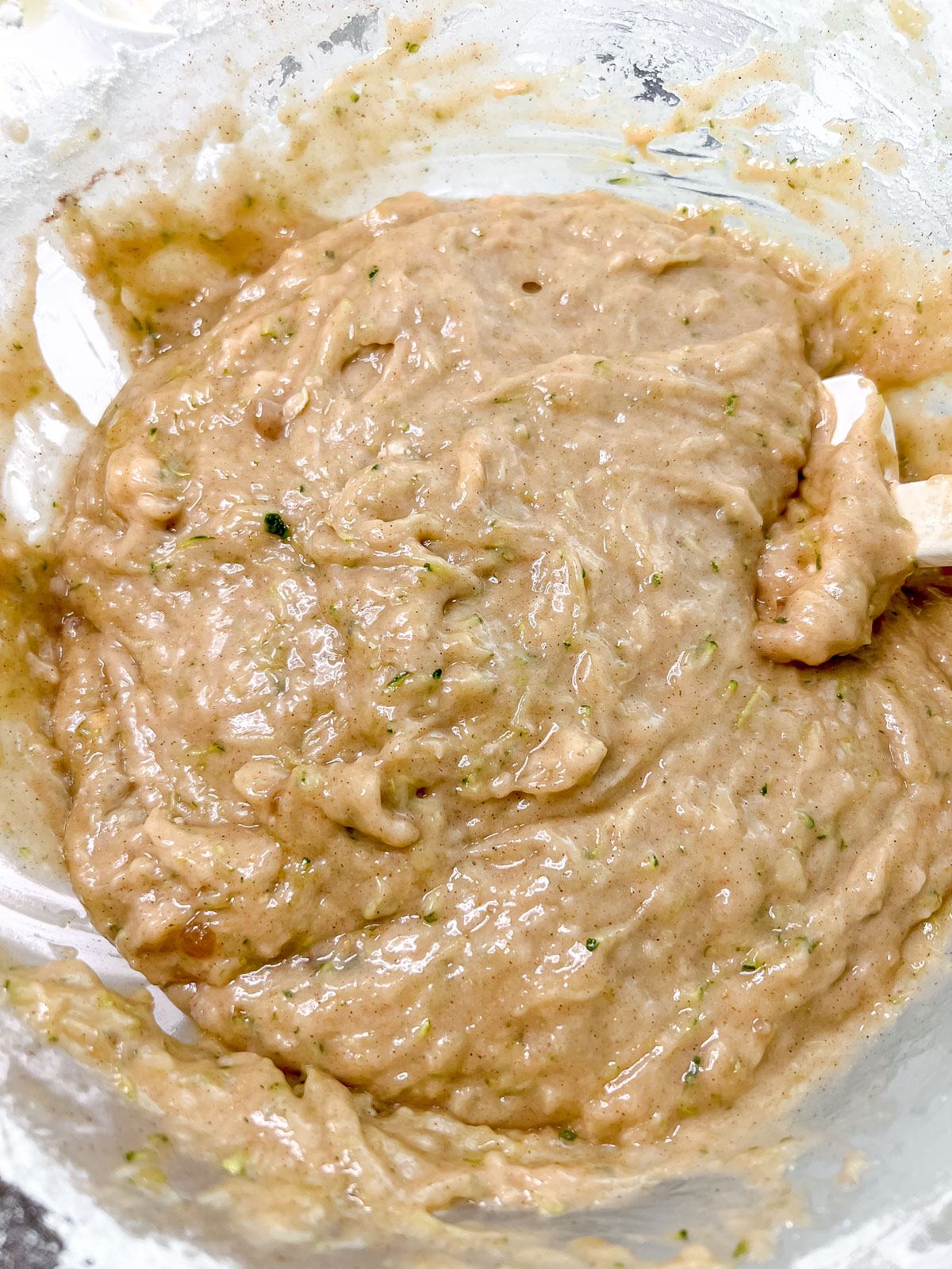 In a clear bowl the zucchini bread batter with a spatula in it. 
