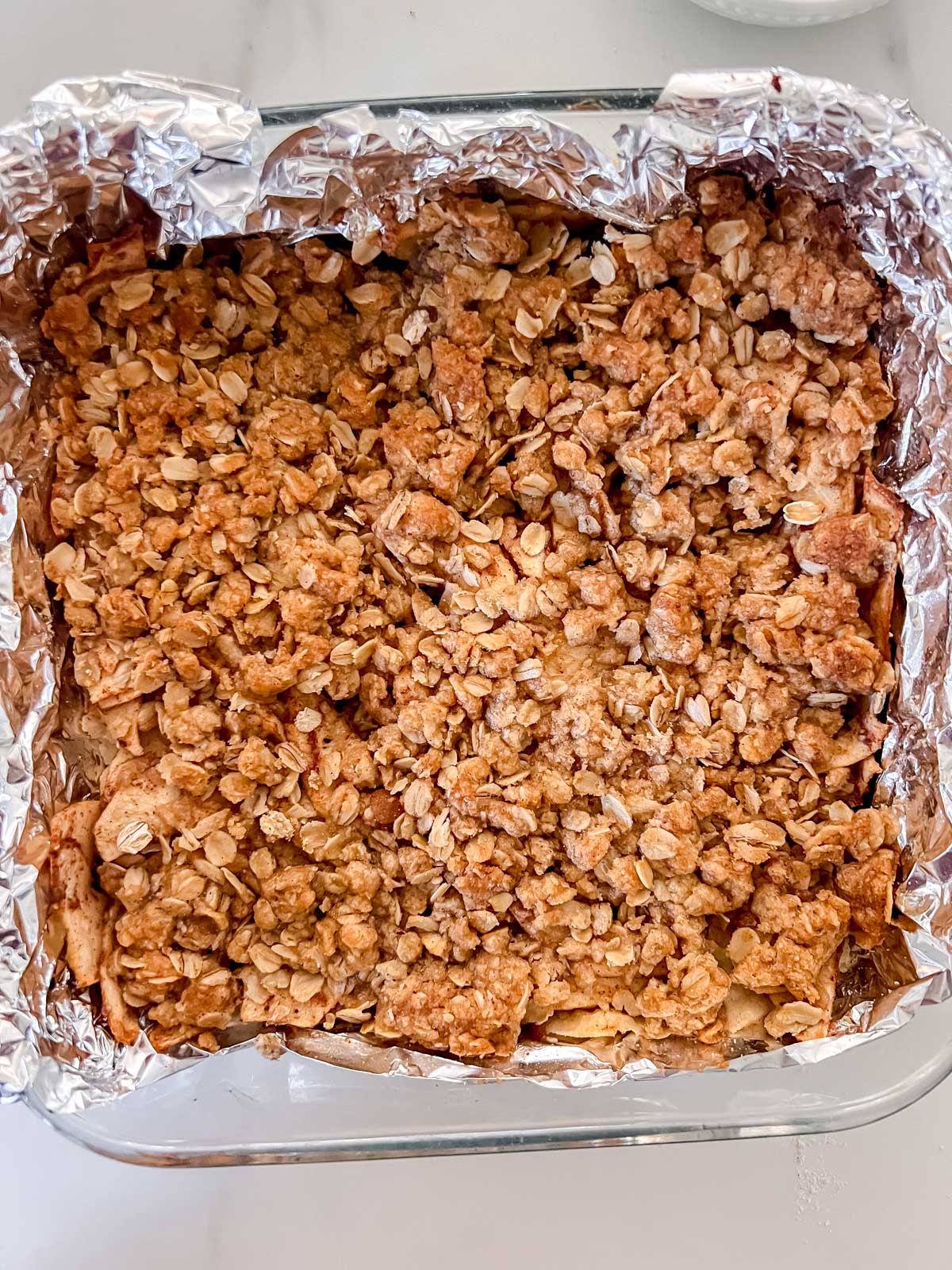 The vegan apple pie bars cooked in an 8x8 pan with foil covering the pan. 