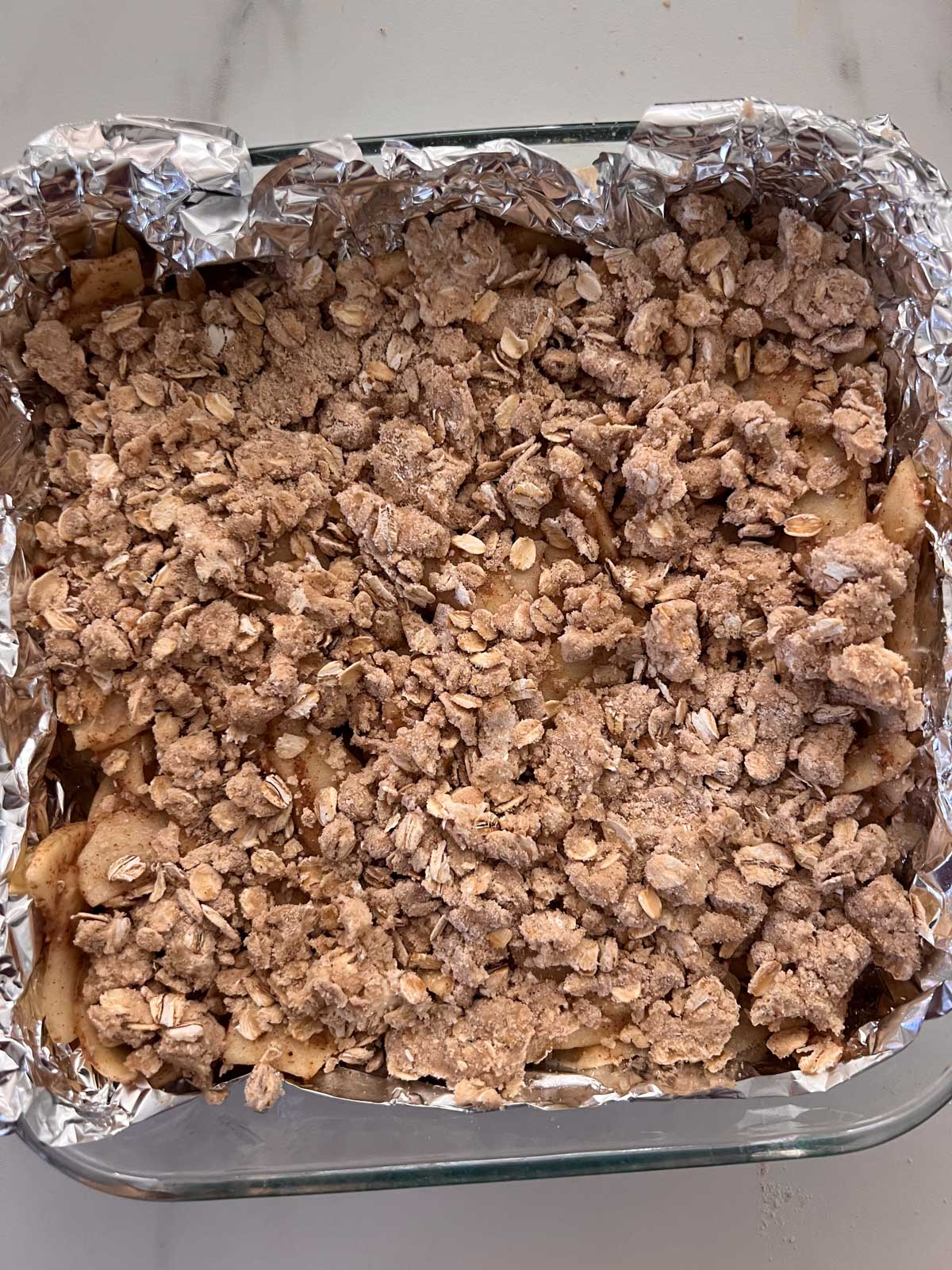 The vegan apple pie bars uncooked in an 8x8 pan with foil covering the pan. 