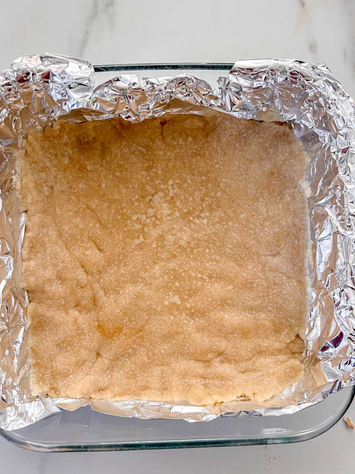 The vegan shortbread crust cooked in an 8x8 pan with foil covering the pan. 