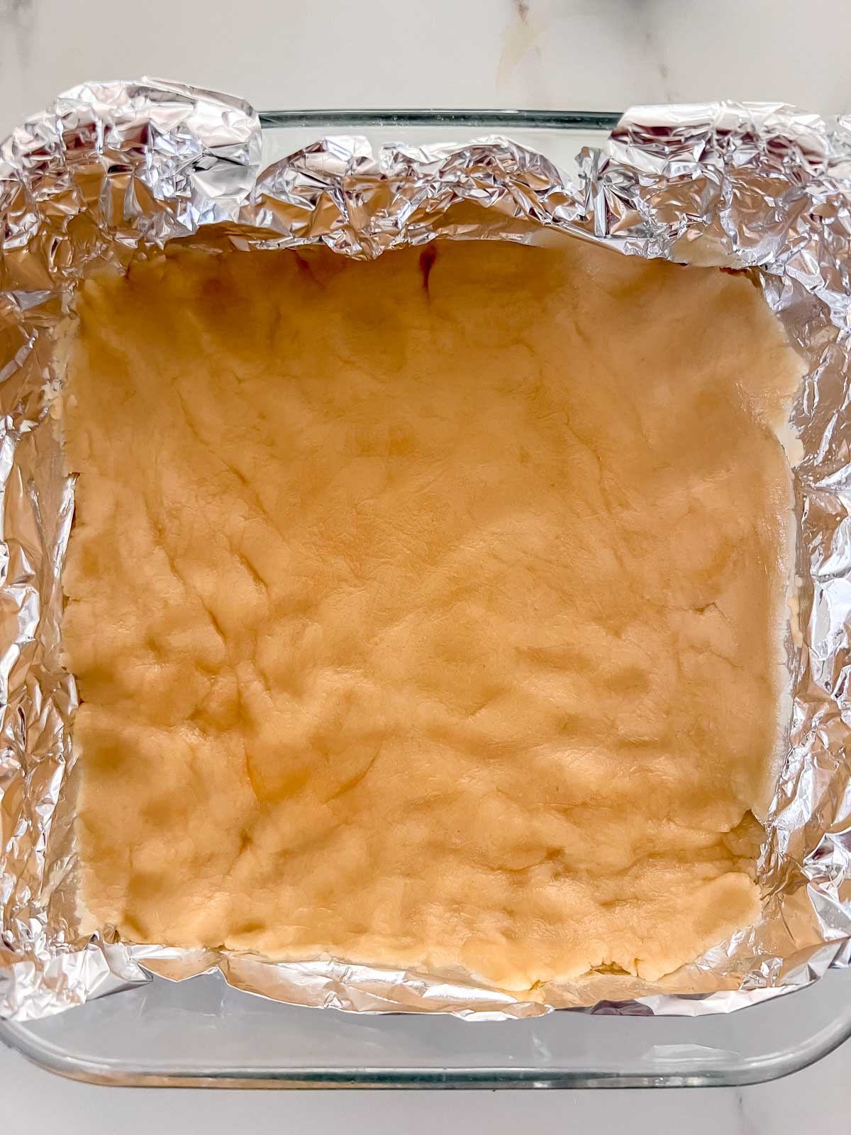 The vegan shortbread crust uncooked in an 8x8 pan with foil covering the pan. 