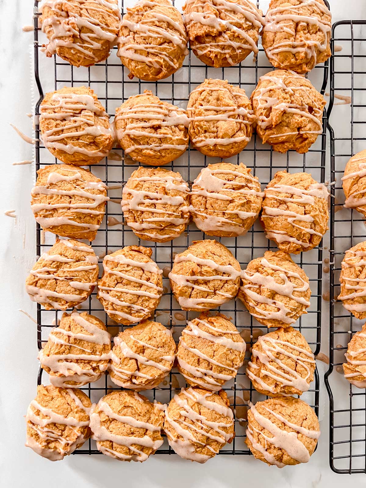 Baked vegan pumpkin cookies on a black cooling rack with a drizzle of cinnamon icing. 