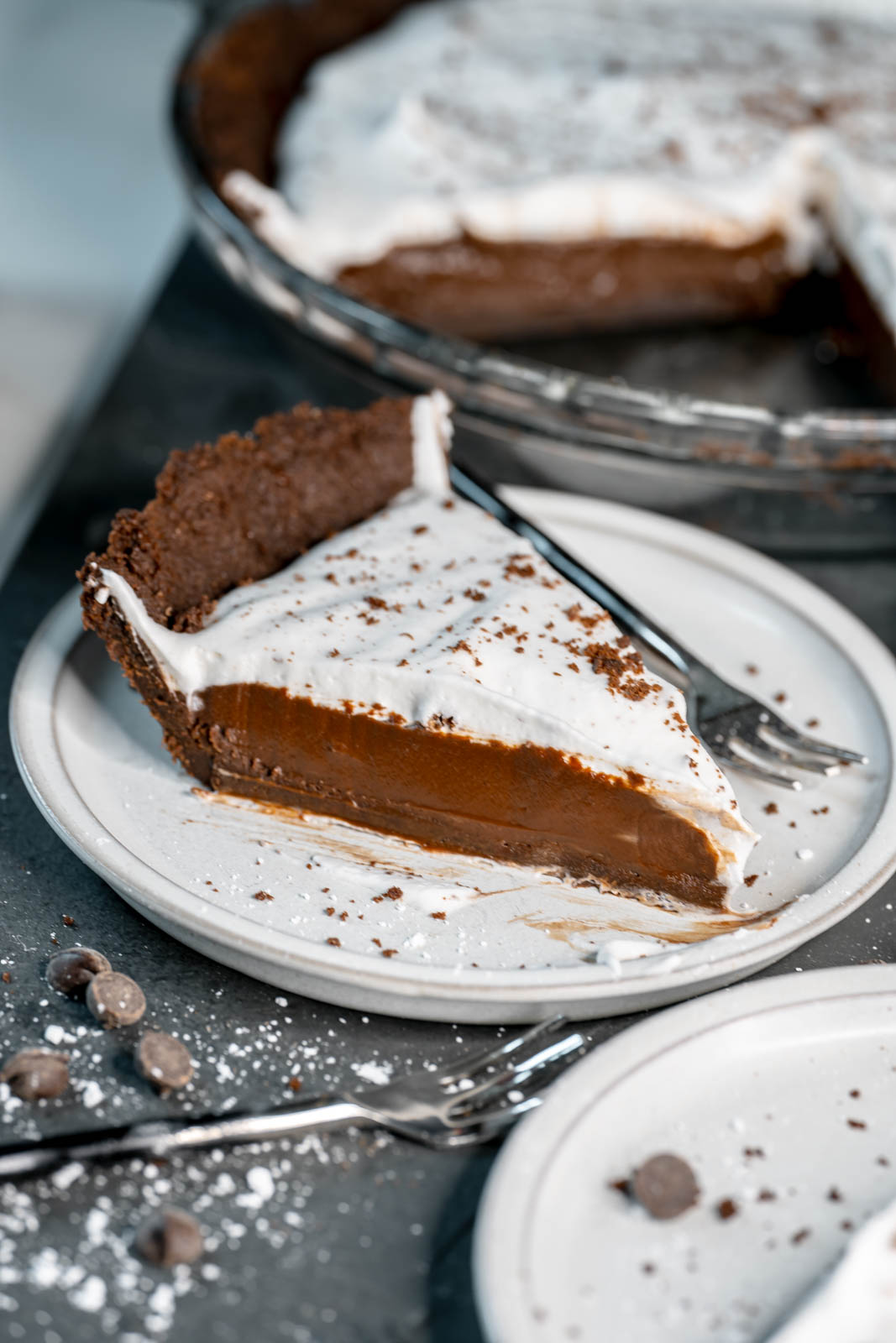 A single slice of vegan chocolate cream pie on a white plate with a small fork. 