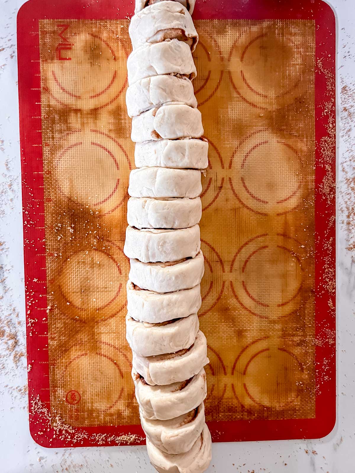 The cinnamon roll dough rolled up in a long roll on a silpat cut into small pieces. 