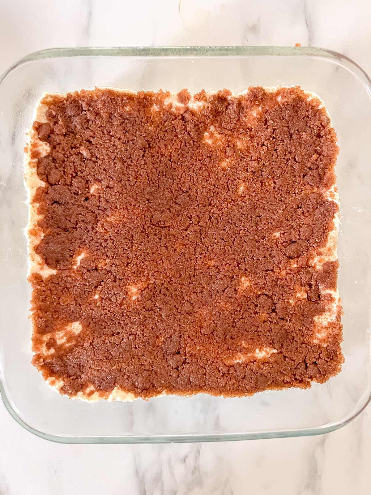 An 8x8 glass pan with half the dough pressed in it with a cinnamon sugar topping on it. 