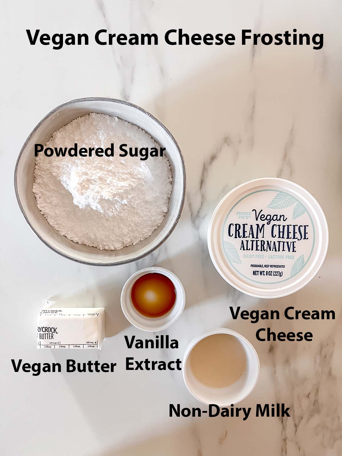 Vegan Cream Cheese frosting ingredients in small bowls with black labels on a marble background. 