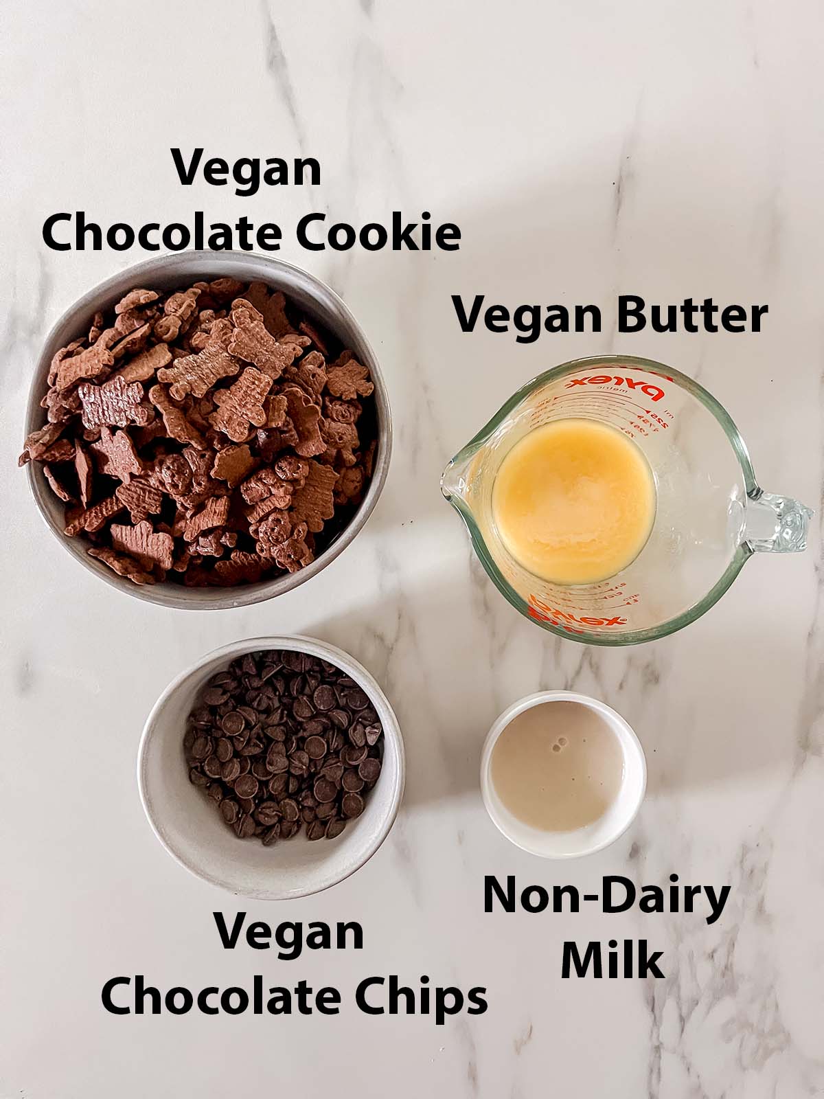 Vegan chocolate cookie crust ingredients in small bowls with black labels on a marble background. 