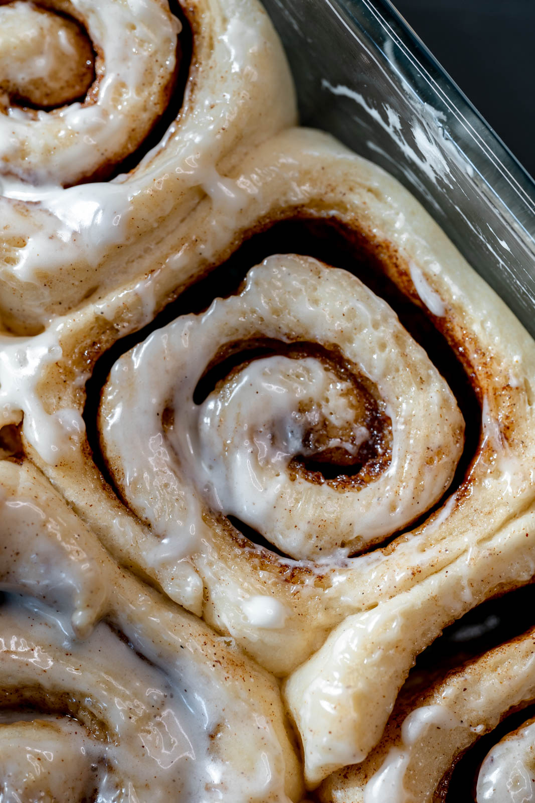 Close up of a vegan cinnamon roll in a glass pan squished with other vegan cinnamon rolls. 