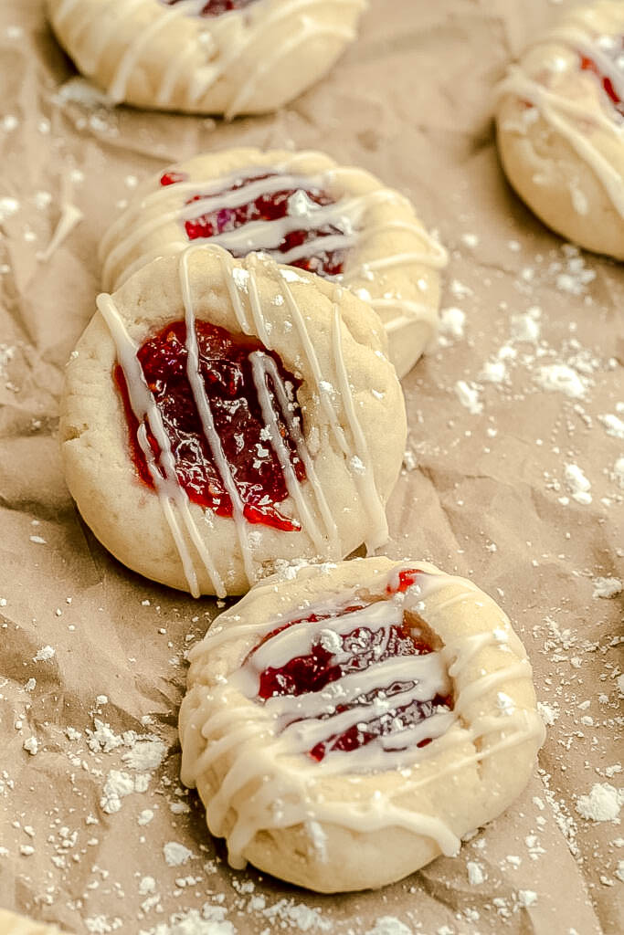 Three vegan thumbprint cookies on a brown paper bag with powdered sugar sprinkled. 