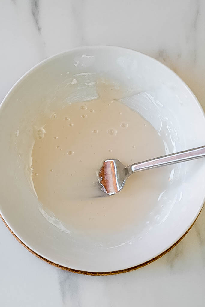 A white bowl with icing and a fork in the middle of the bowl. 