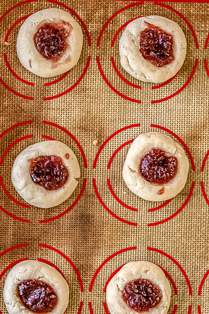 Vegan thumbprint cookies with jam in them after being baked on a silpat pan. 