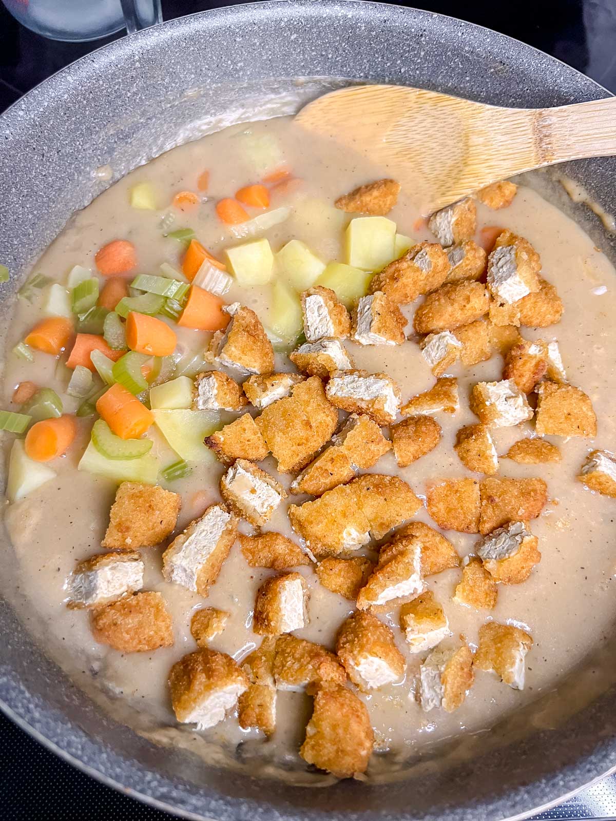 Adding the vegan chicken, and vegetables to the vegan gravy in a pot. 