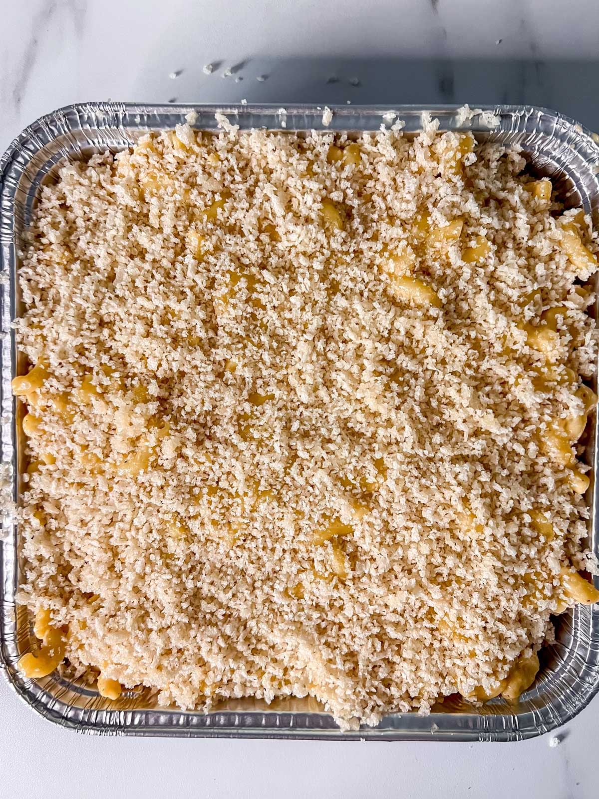 A silver 8x8 pan with the vegan mac and cheese with panko breadcrumbs on top before going into the oven. 