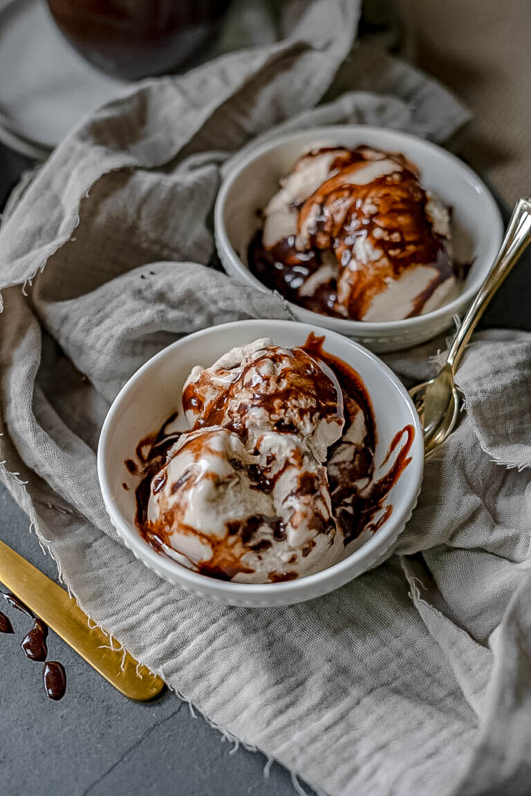 Two bowls of vegan vanilla ice cream with vegan chocolate sauce drizzled and melted into it. 