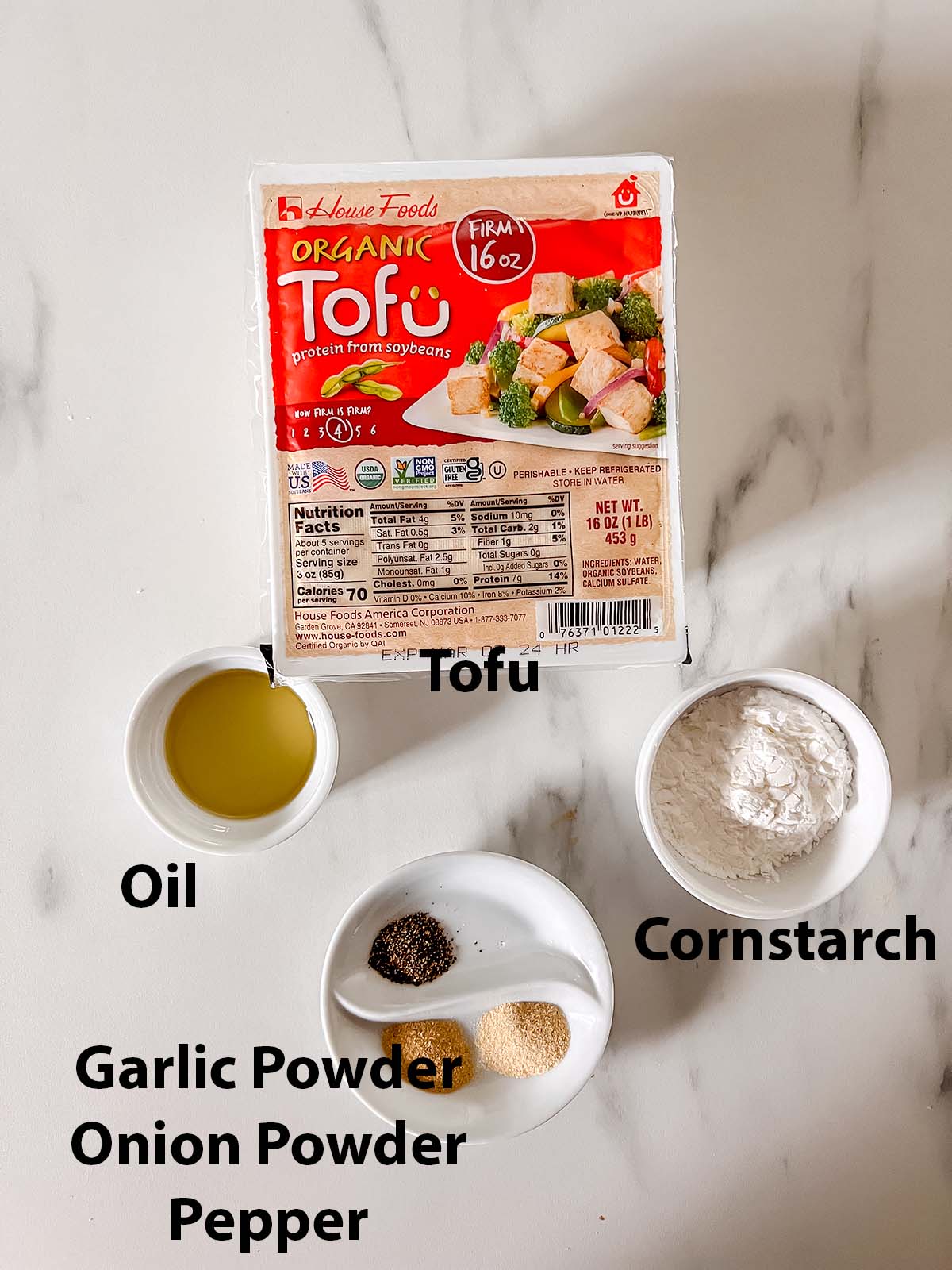 The tofu ingredients in small bowls with black writing labels on a marble background. 